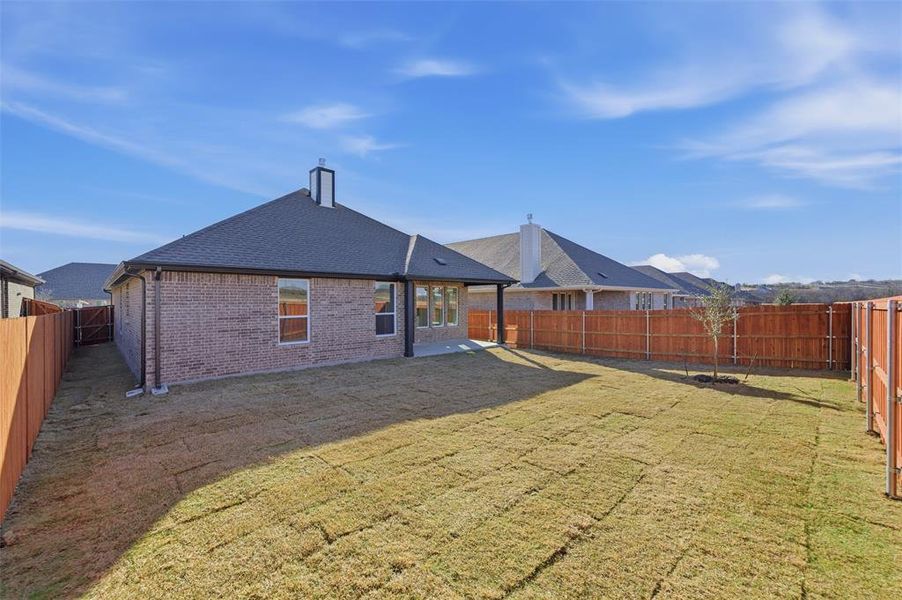 Rear view of property featuring a fenced backyard, a patio, brick siding, and roof with shingles