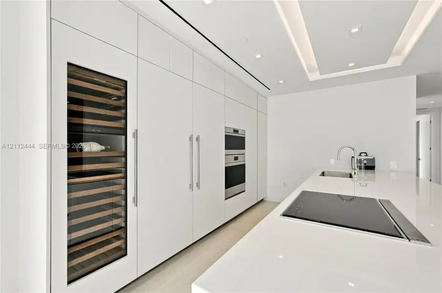 Sleek kitchen featuring custom floor-to-ceiling cabinetry, built-in stainless steel appliances, a glass-front wine refrigerator, and a solid-surface island with an integrated cooktop and undermount sink