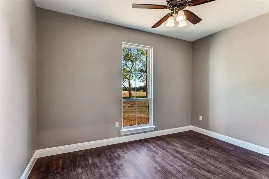 Unfurnished room featuring dark wood-type flooring and a ceiling fan Unfurnished room featuring dark wood-type flooring and a ceiling fan