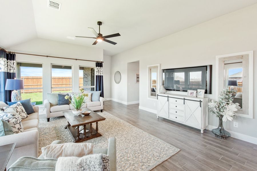 Living room with vaulted ceiling, ceiling fan, hardwood floors, and white media console with wall-mounted TV