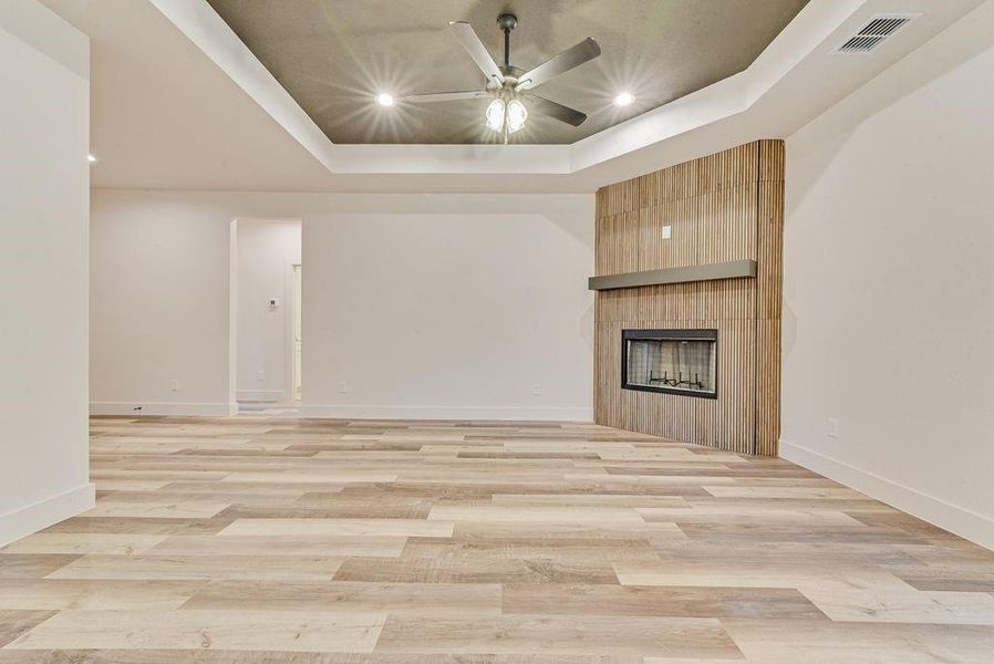 Unfurnished living room featuring a raised ceiling, a fireplace, recessed lighting, light wood finished floors, and ceiling fan Unfurnished living room featuring a raised ceiling, a fireplace, recessed lighting, light wood finished floors, and ceiling fan