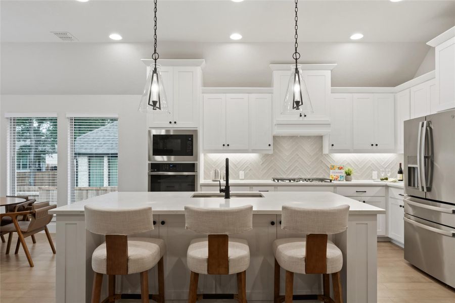 Contemporary kitchen featuring a large central island, white cabinetry, stainless steel appliances, and herringbone tile backsplash