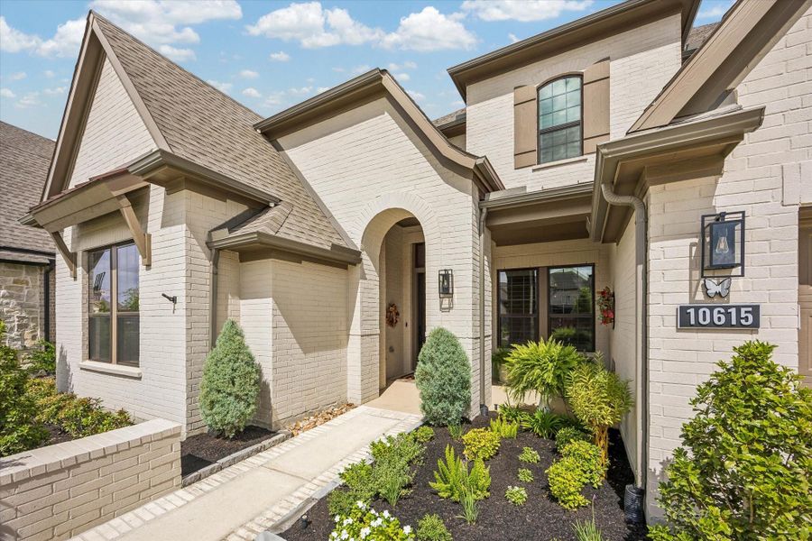 The paver lined walkway leads to a lovely covered front porch. The home features painted brick, gutters and lush landscaping throughout.