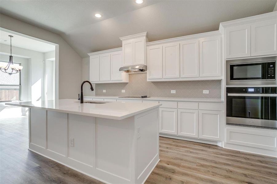 Kitchen featuring white cabinets, sink, light wood-type flooring, tasteful backsplash, and stainless steel appliances