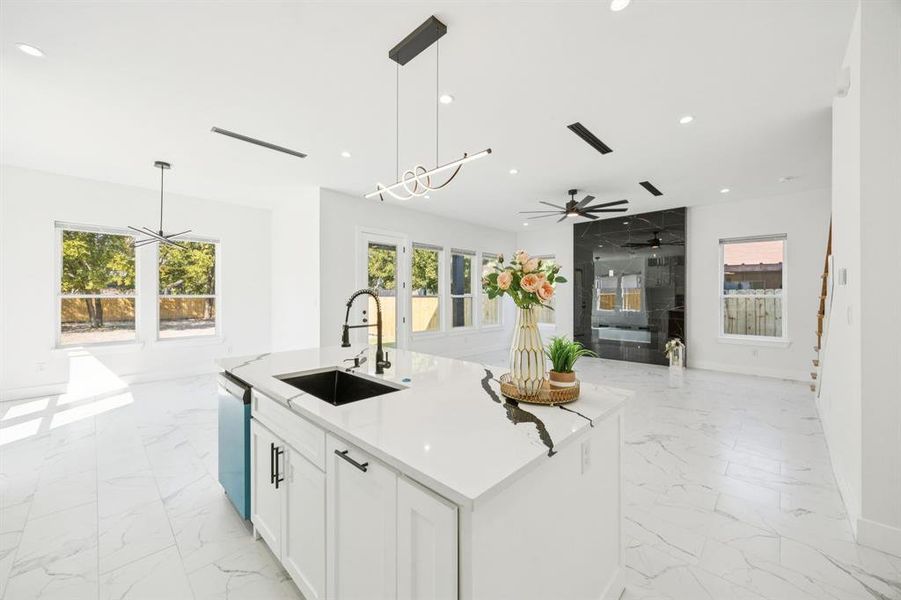Kitchen with open floor plan, white cabinetry, light stone counters, hanging light fixtures, and light marble finish flooring