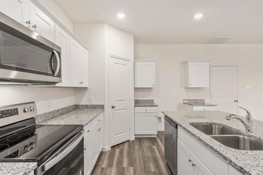 Kitchen with appliances with stainless steel finishes, white cabinetry, dark wood-style floors, light stone counters, and recessed lighting Kitchen with appliances with stainless steel finishes, white cabinetry, dark wood-style floors, light stone counters, and recessed lighting