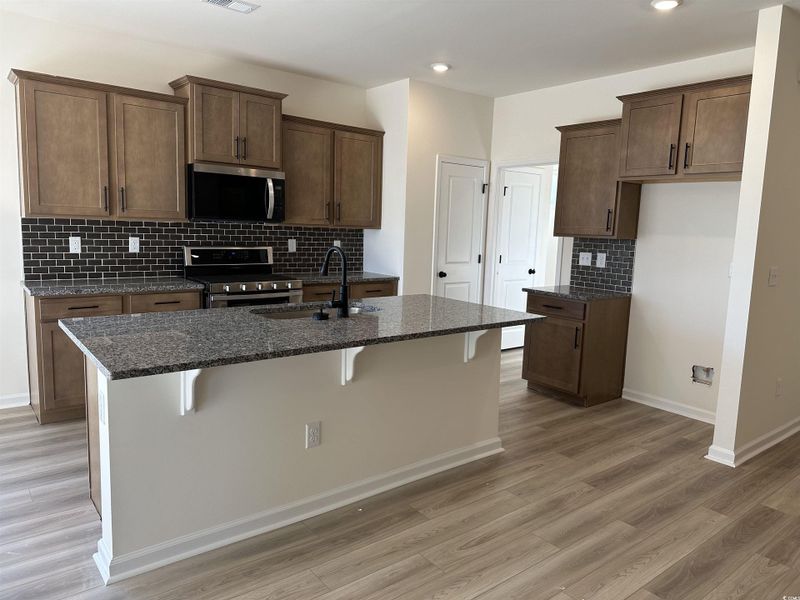 Kitchen featuring dark stone counters, backsplash, a breakfast bar area, stainless steel appliances, and an island with sink