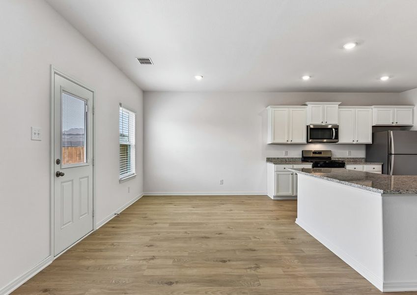 Kitchen featuring a granite island, white cabinetry, and stainless steel appliances with wood-look vinyl flooring.