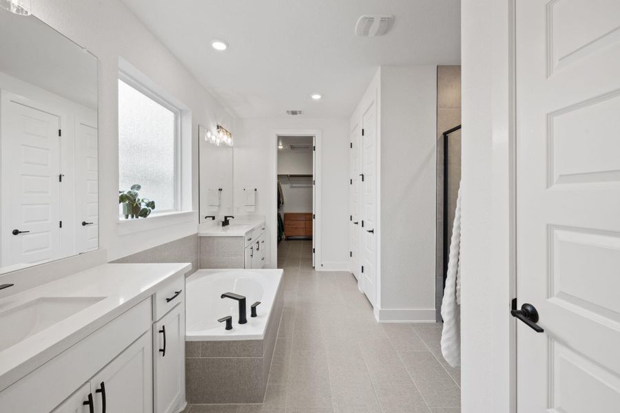 Main level master bathroom with two vanities, a spacious closet, a garden tub, quartz countertops, a shower stall, and recessed lighting.
