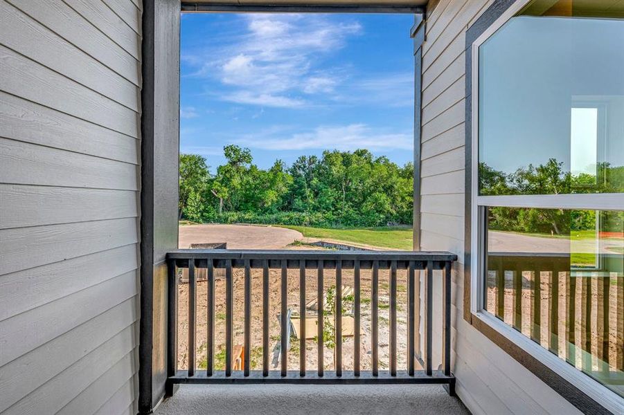 Outdoor balcony featuring slatted wood siding, a dark railing, and an expansive window