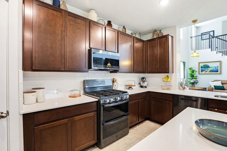 Kitchen featuring dark wood cabinetry, white countertops, a subway tile backsplash, and stainless steel appliances including a gas range and built-in microwave