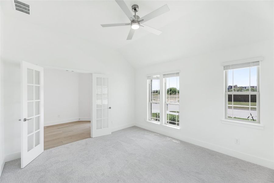Empty bedroom with gray carpet, ceiling fan, French doors, and multiple windows with outdoor views