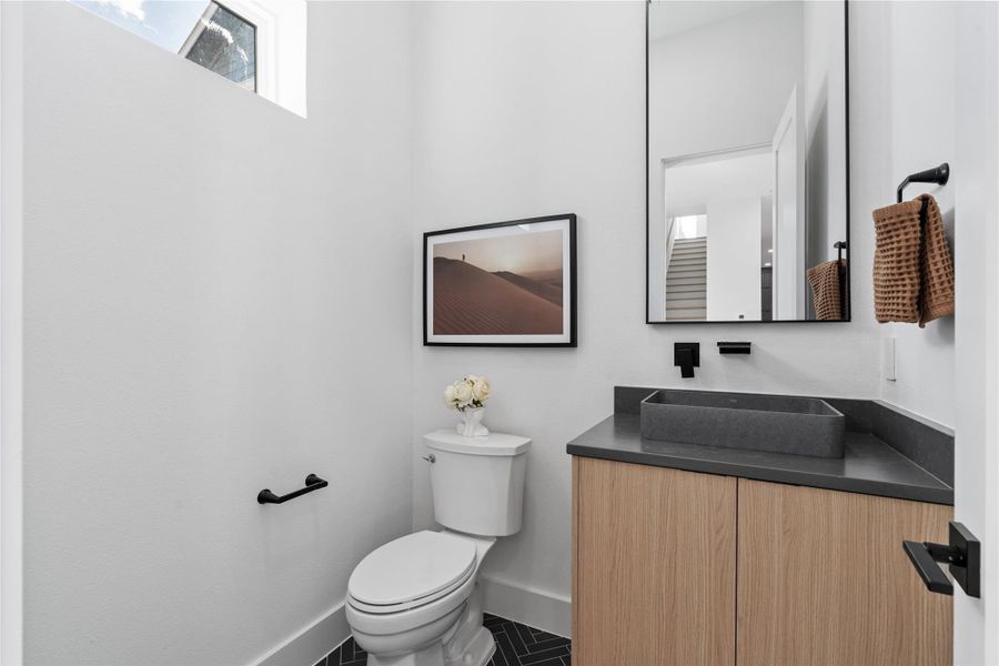 A meticulously composed powder room where form follows precision: clerestory light skims crisp walls, a graphite-hued vessel sink rests on tailored wood cabinetry, and matte-black fixtures punctuate the palette. The herringbone floor adds quiet movement underfoot—an elegant, guest-facing moment that reflects the home’s considered craftsmanship. A meticulously composed powder room where form follows precision: clerestory light skims crisp walls, a graphite-hued vessel sink rests on tailored wood cabinetry, and matte-black fixtures punctuate the palette. The herringbone floor adds quiet movement underfoot—an elegant, guest-facing moment that reflects the home’s considered craftsmanship.