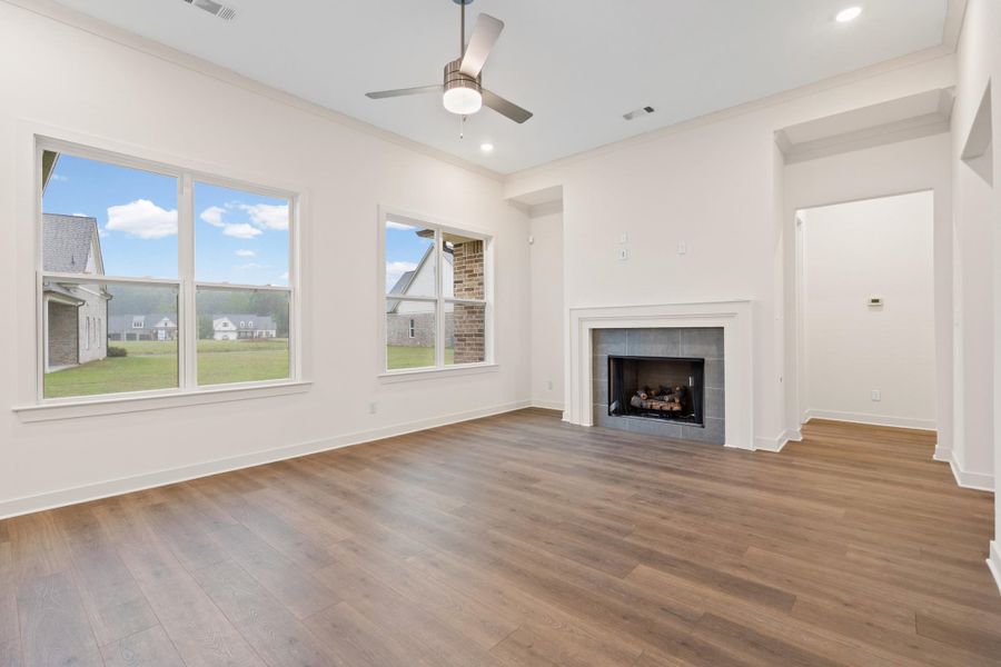 Open-concept living space featuring wood-finish flooring, a contemporary fireplace with a dark tile surround, multiple windows, recessed lighting, and a ceiling fan Open-concept living space featuring wood-finish flooring, a contemporary fireplace with a dark tile surround, multiple windows, recessed lighting, and a ceiling fan