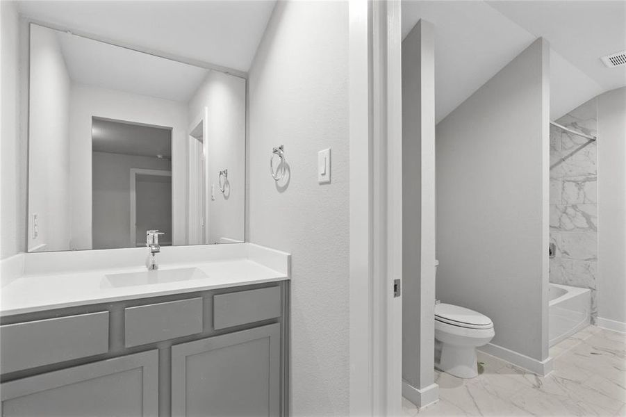 Secondary bath features tile flooring, bath/shower combo with tile surround, stained wood cabinets, beautiful light countertops, mirror, sleek fixtures and modern finishes.