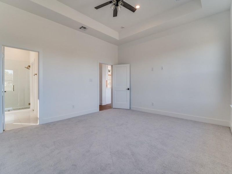 Unfurnished bedroom featuring a raised ceiling, light colored carpet, and ceiling fan