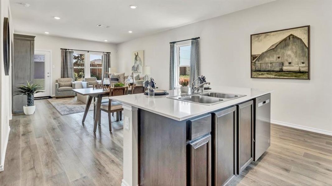 Open-concept living space featuring wood-finish flooring, recessed lighting, and a kitchen island with dual sinks and stainless steel appliances Open-concept living space featuring wood-finish flooring, recessed lighting, and a kitchen island with dual sinks and stainless steel appliances