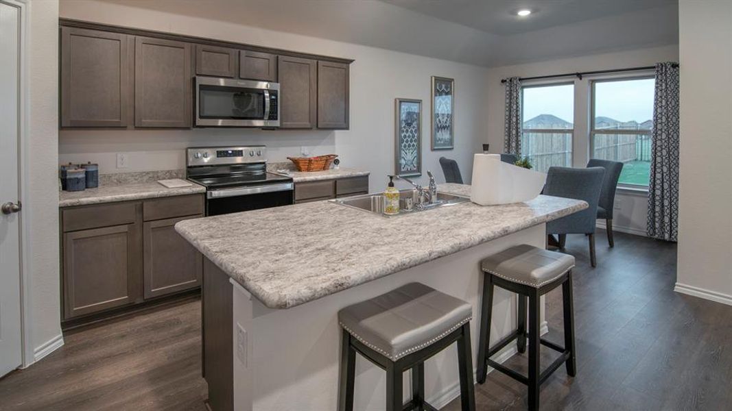 Kitchen featuring a breakfast bar area, light countertops, stainless steel appliances, dark wood-style flooring, and dark wood finish cabinetry