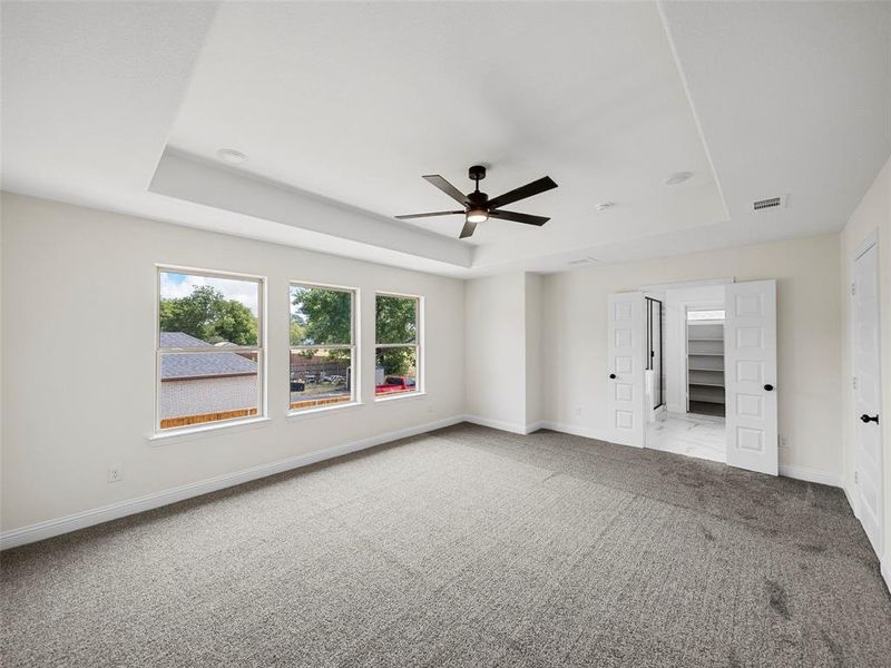 Empty room with ceiling fan, a tray ceiling, and light carpet