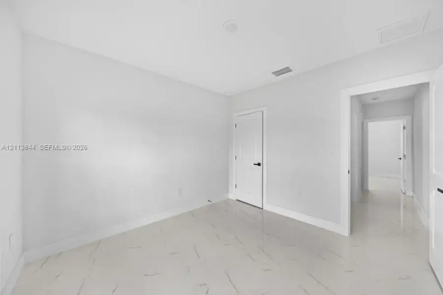 Interior room featuring polished stone-finish tile flooring, neutral wall tones, white panel doors with matte black hardware, and recessed ceiling lighting Interior room featuring polished stone-finish tile flooring, neutral wall tones, white panel doors with matte black hardware, and recessed ceiling lighting