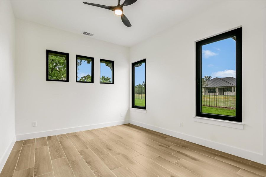 Spacious room featuring wood-finish flooring, white walls, and multiple black-framed windows