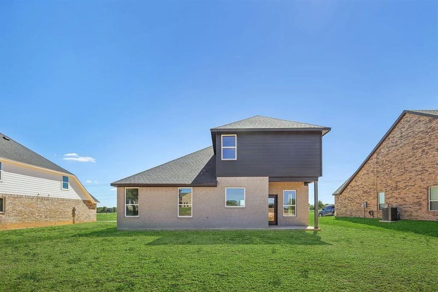 Rear view of property with a lawn, a patio, roof with shingles, and central AC unit