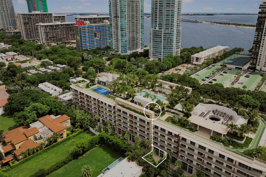 Aerial perspective featuring a multi-story residential building with a landscaped rooftop pool, recreational court, and ground-level private garden area Aerial perspective featuring a multi-story residential building with a landscaped rooftop pool, recreational court, and ground-level private garden area