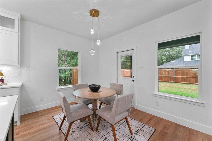 Dining area featuring wood-finish flooring, a contemporary three-light pendant fixture, and white cabinetry with a quartz countertop and subway tile backsplash Dining area featuring wood-finish flooring, a contemporary three-light pendant fixture, and white cabinetry with a quartz countertop and subway tile backsplash