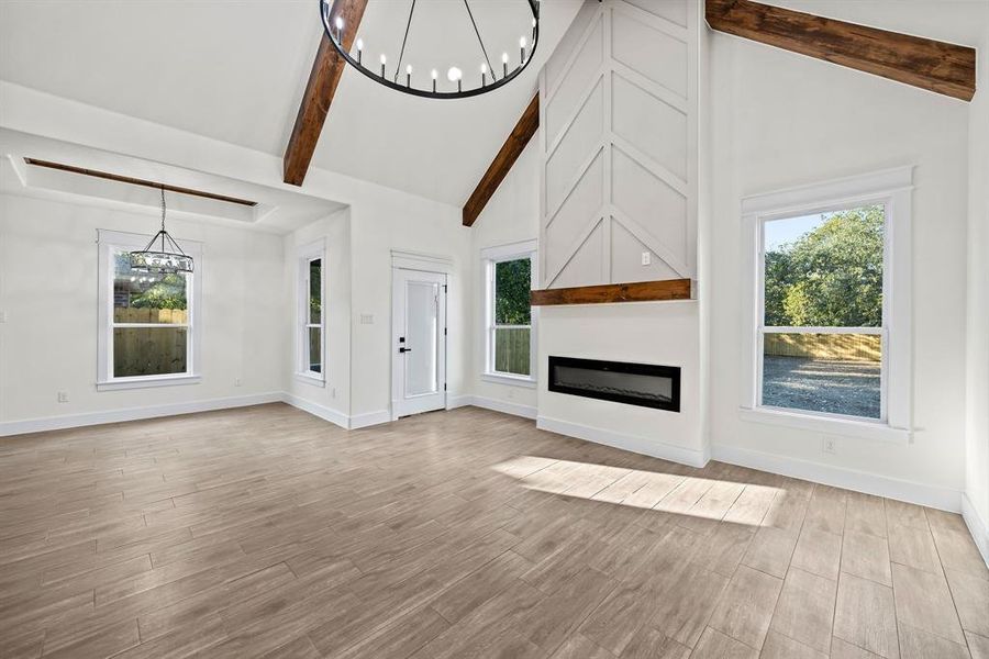 Unfurnished living room with a chandelier, a glass covered fireplace, beam ceiling, high vaulted ceiling, and light wood-style flooring