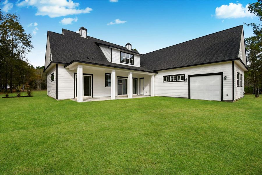 The back of the home is designed for indoor-outdoor living, featuring a spacious covered patio and multiple sliding glass doors that overlook the sprawling green lawn.