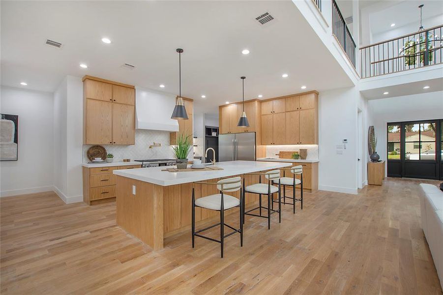 Kitchen featuring custom exhaust hood, a spacious island, light hardwood / wood-style flooring, light brown cabinetry, and high end refrigerator