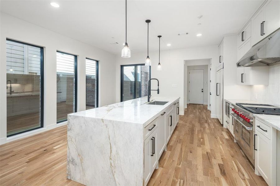 Kitchen with light stone counters, white cabinetry, sink, and an island with sink