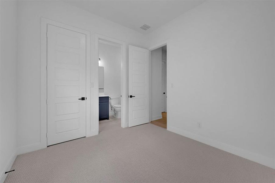 Unfurnished bedroom with light colored carpet and connected bathroom