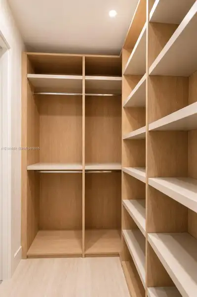 Customized reach-in closet featuring light wood-finish cabinetry, built-in shelving units, integrated metal hanging rods, and recessed ceiling lighting