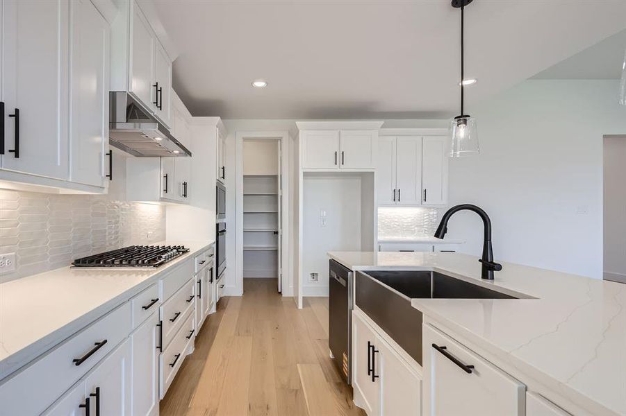 Kitchen with under cabinet range hood, a sink, stainless steel appliances, white cabinets, and light wood finished floors Kitchen with under cabinet range hood, a sink, stainless steel appliances, white cabinets, and light wood finished floors