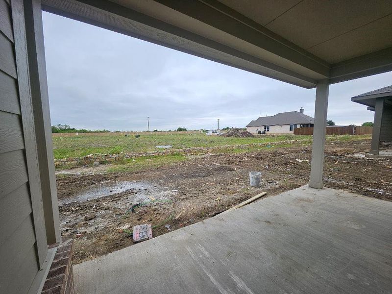 Covered concrete patio with a painted ceiling, supported by square columns, offering an open expanse of undeveloped land beyond Covered concrete patio with a painted ceiling, supported by square columns, offering an open expanse of undeveloped land beyond