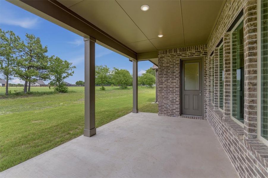Covered concrete patio featuring recessed lighting, a brick exterior wall, and a rear entry door