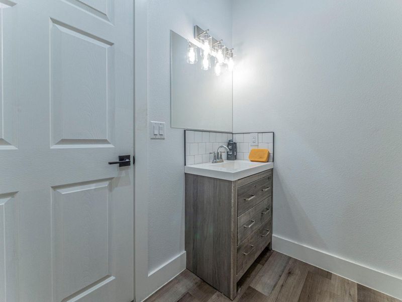 Bathroom with tasteful backsplash, vanity, light wood-type flooring, and a textured wall