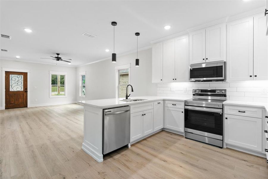 Kitchen with stainless steel appliances, light wood-style floors, a peninsula, tasteful backsplash, and recessed lighting