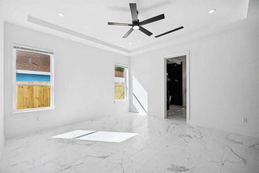 Empty room featuring light marble finish floors, a tray ceiling, recessed lighting, and ceiling fan