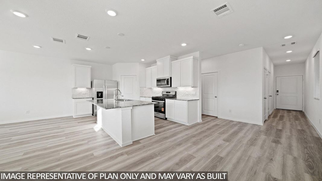 Open-concept kitchen and living area featuring wood-finish flooring, white cabinetry, a kitchen island with stone countertops, stainless steel appliances, and recessed lighting