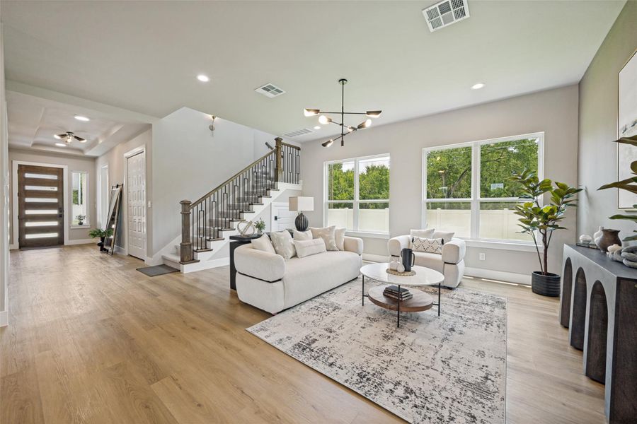 An inviting open-concept living space features light wood flooring and a modern chandelier, creating an airy ambiance.