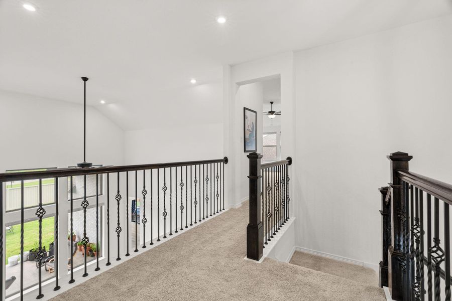 An open second-story landing features elegant wrought iron railings, vaulted ceilings, and plush carpeting. An open second-story landing features elegant wrought iron railings, vaulted ceilings, and plush carpeting.