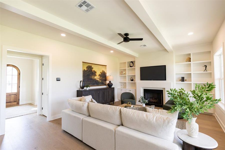 Living area featuring a fireplace with a mantel, built-in shelving, wood-finish flooring, and a ceiling fan
