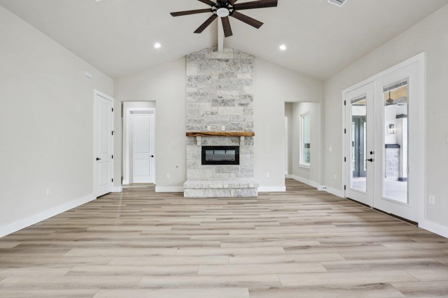 Unfurnished living room with french doors, a ceiling fan, and a stone fireplace