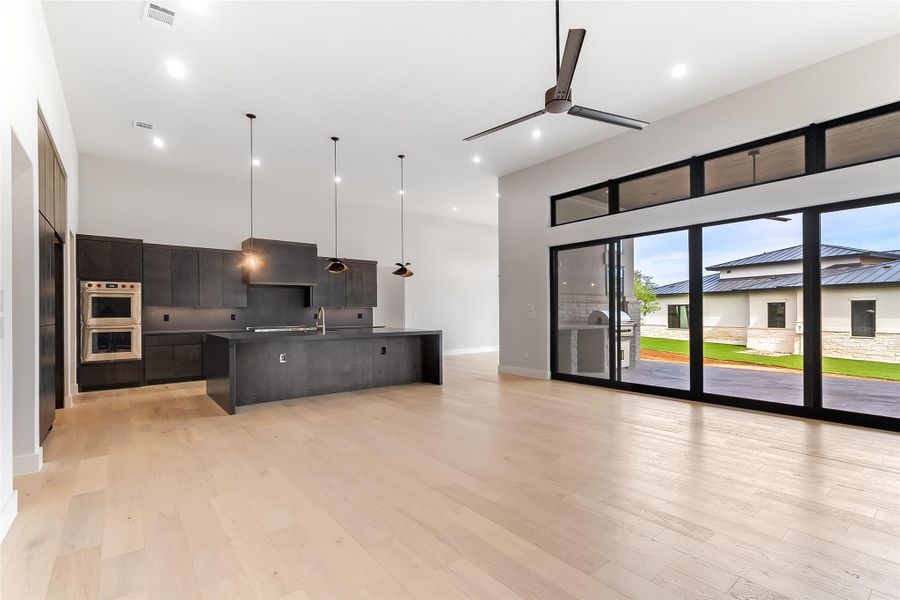 Unfurnished living room with a ceiling fan, a sink, light wood-type flooring, a high ceiling, and baseboards Unfurnished living room with a ceiling fan, a sink, light wood-type flooring, a high ceiling, and baseboards