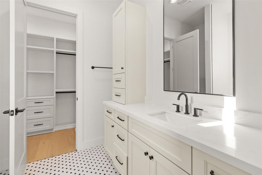 This well-appointed secondary bathroom pairs timeless style with everyday function. A spacious vanity topped with quartz counters offers ample storage, complete with a full-height cabinet tower and abundant drawers to keep everything organized. Classic black-and-white penny tile flooring adds a charming, characterful touch, while sleek matte black fixtures and hardware deliver a clean, modern contrast.