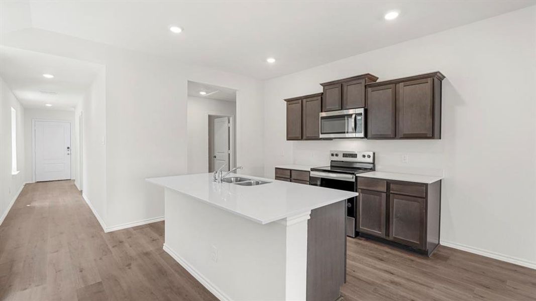 Modern kitchen featuring a central island with an integrated double sink, white countertops, and dark wood-finish cabinetry