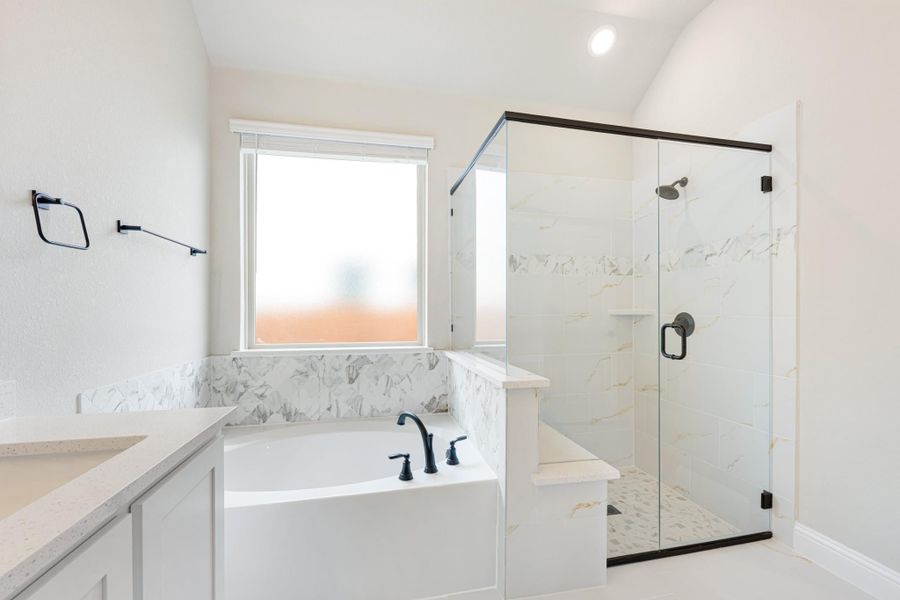 Master bathroom with soaking tub, glass-enclosed shower, marble tile, and white vanity with quartz countertop