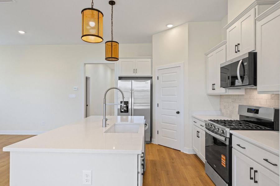Modern kitchen featuring an expansive island with an integrated sink, white cabinetry, stainless steel appliances, and wood-finish flooring Modern kitchen featuring an expansive island with an integrated sink, white cabinetry, stainless steel appliances, and wood-finish flooring